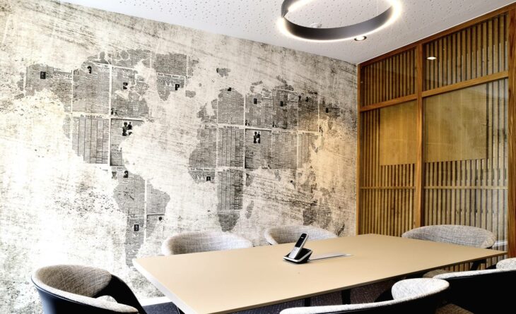 a room with one wooden wall and a wall with wallpaper of two continents. there is a desk with six chairs and a telephone in the middle of the desk