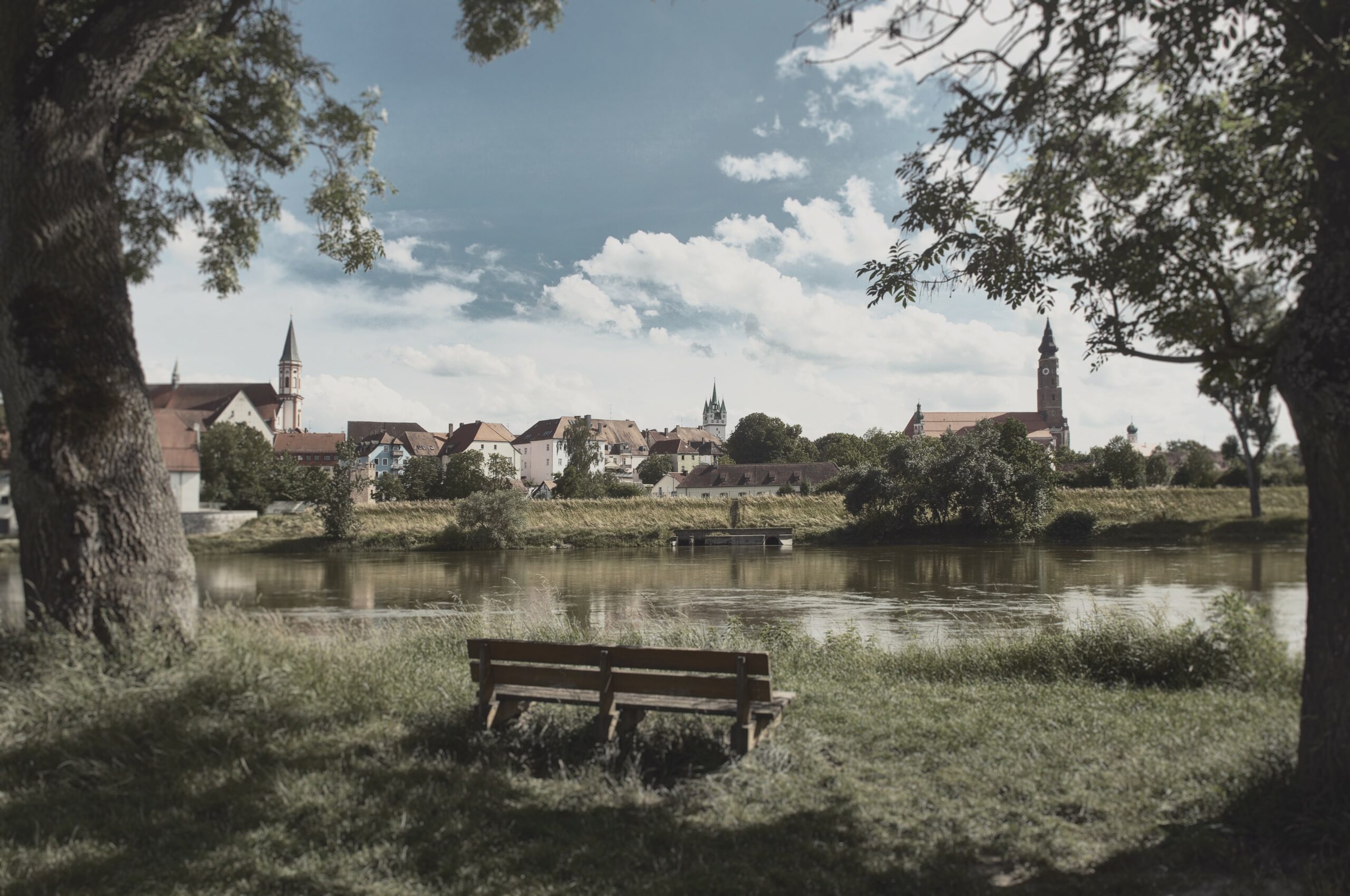 a picture of a bench on grass. the danube is in front of it and you can see the city Straubing in the background