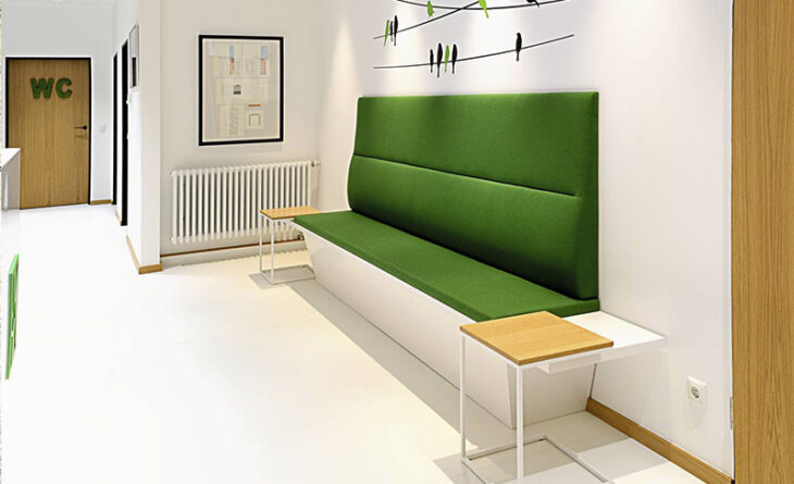 a white room with a green couch. there are two tables on each side of the couch and a heating right next to it